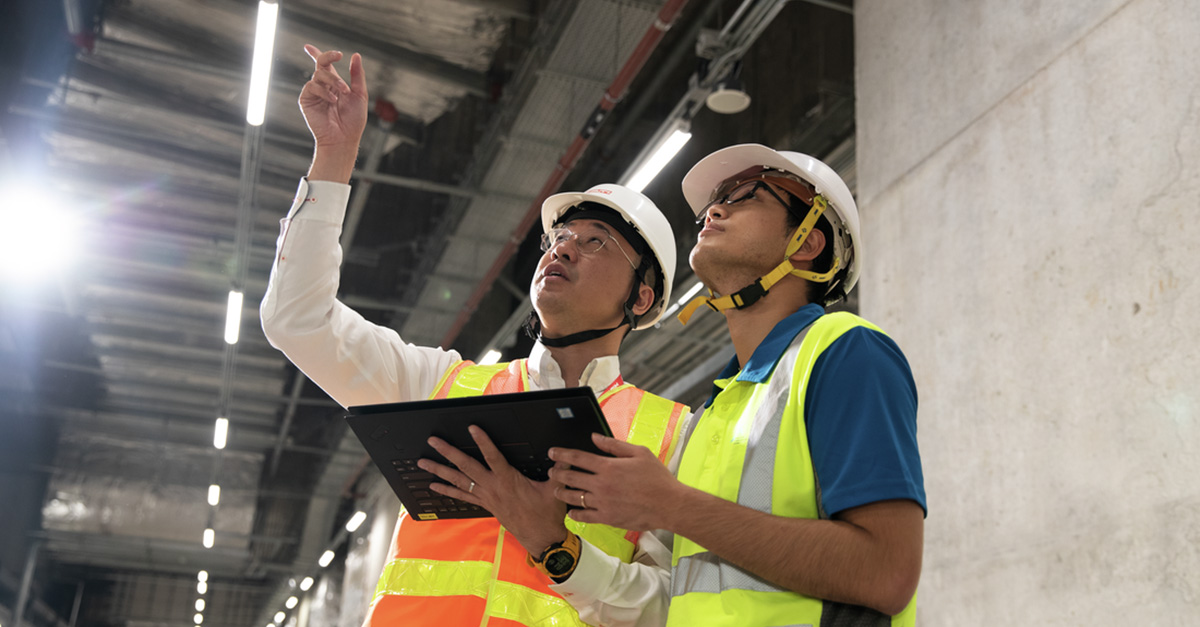 Two construction workers talking on jobsite while holding tablet.