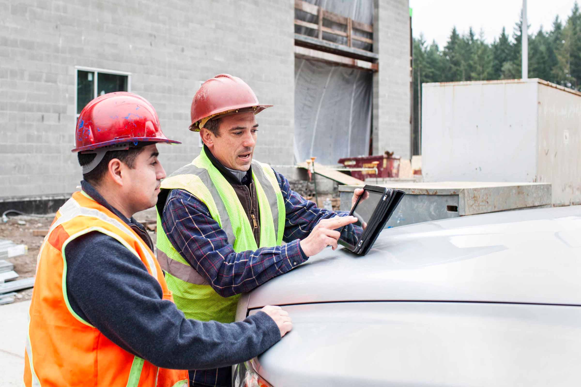 Two construction workers looking at construction software on a tablet on a project jobsite.